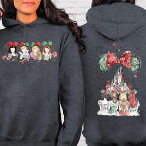 May include: Dark gray hoodie featuring a colorful illustration of Disney princesses on the front and back. The front design shows four princesses with candy canes and mouse ears. The back features a castle and mouse ears with a red bow.