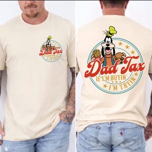 May include: Cream-colored t-shirt featuring a cartoon character holding a burger and fries, with the text "Dad Tax" and "If I'm Buyin' I'm Tryin'". The design is printed on the front and back of the shirt.