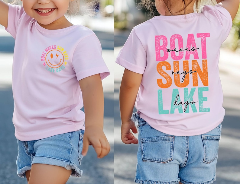 May include: A light pink t-shirt featuring the text "Boat Waves Lake Days" and a smiling sun graphic on the front. The back of the shirt displays "Boat Waves Sun Rays Lake Days" in colourful block letters. The child is wearing blue denim shorts.