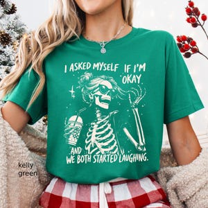 May include: Kelly green t-shirt featuring a skeleton graphic wearing sunglasses and holding a beverage. The text on the shirt reads, "I ASKED MYSELF IF I'M OKAY AND WE BOTH STARTED LAUGHING."