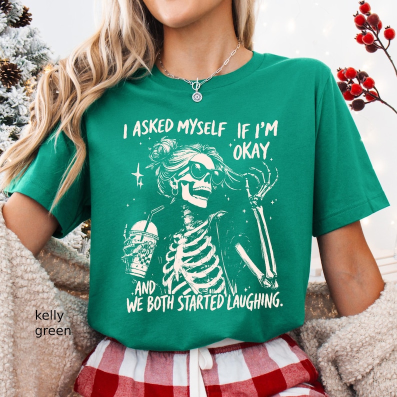 May include: Kelly green t-shirt featuring a skeleton graphic wearing sunglasses and holding a beverage. The text on the shirt reads, "I ASKED MYSELF IF I'M OKAY AND WE BOTH STARTED LAUGHING."