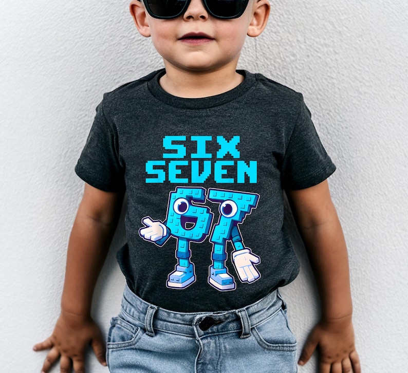 May include: Dark gray t-shirt with the words "SIX SEVEN" in pixelated blue letters. Below, the numbers "67" are depicted as cartoon characters with blue bodies, white gloves, and blue shoes. The shirt is worn by a child.