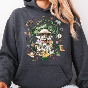 Peut inclure: Sweat &agrave; capuche gris fonc&eacute; avec un motif color&eacute; de personnages Disney en tenue de safari. Le design comprend Mickey Mouse, Donald Duck et Dingo, entour&eacute;s d'&eacute;l&eacute;ments sur le th&egrave;me du safari comme une boussole, des jumelles et un chapeau de safari. Le sweat &agrave; capuche a une poche kangourou et une capuche &agrave; cordon.