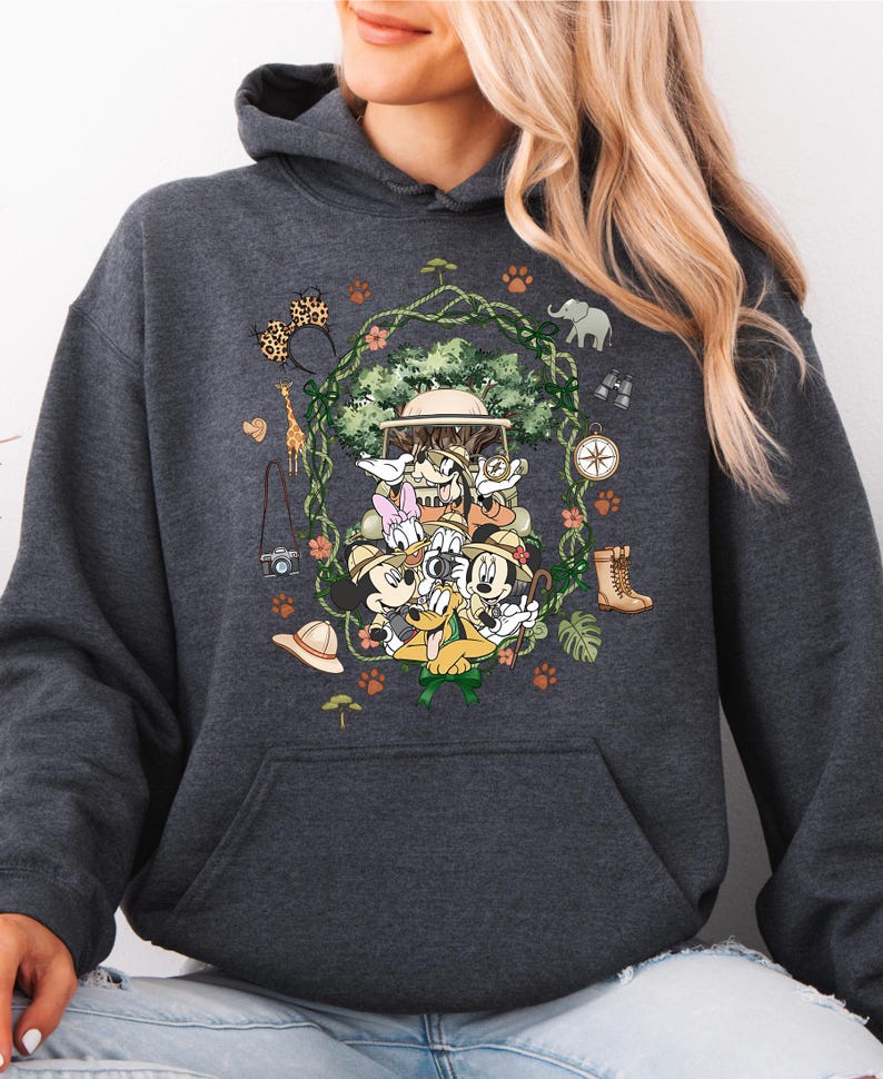Peut inclure: Sweat &agrave; capuche gris fonc&eacute; avec un motif color&eacute; de personnages Disney en tenue de safari. Le design comprend Mickey Mouse, Donald Duck et Dingo, entour&eacute;s d'&eacute;l&eacute;ments sur le th&egrave;me du safari comme une boussole, des jumelles et un chapeau de safari. Le sweat &agrave; capuche a une poche kangourou et une capuche &agrave; cordon.