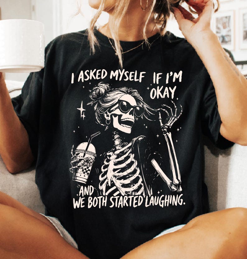May include: Black t-shirt featuring a skeleton wearing sunglasses and holding a drink. The graphic includes the text "I asked myself if I'm okay, and we both started laughing."