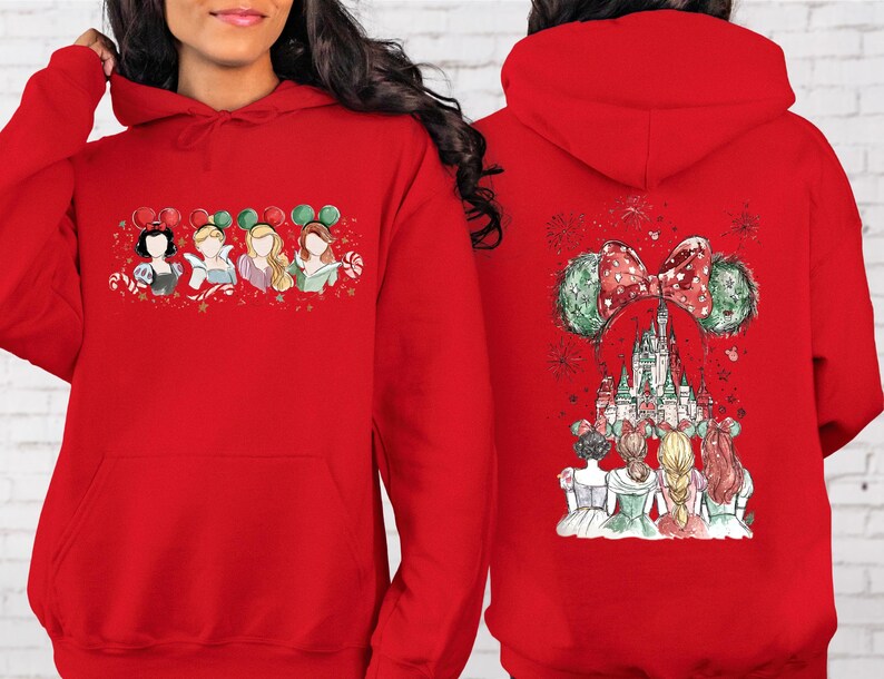 May include: Red hooded sweatshirt featuring a festive design. The front displays four cartoon princesses with mouse ears. The back showcases a castle with a bow and mouse ears. The design incorporates red, green, and white elements.