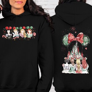 May include: Black hooded sweatshirt featuring a colorful graphic of Disney princesses with holiday-themed Minnie Mouse ears and a castle design. The front shows the princesses, while the back displays the castle and fireworks.
