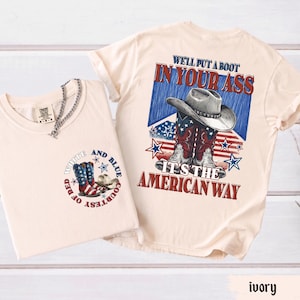May include: An ivory t-shirt featuring a small graphic on the front with cowboy boots and the text "COURTESY OF RED WHITE AND BLUE". The back displays a large graphic of cowboy boots and a hat with the text "WE'LL PUT A BOOT IN YOUR ASS IT'S THE AMERICAN WAY".