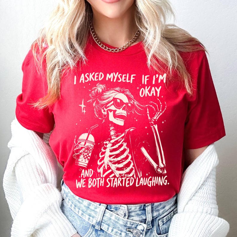 May include: Red t-shirt with a white graphic of a skeleton wearing sunglasses and holding a drink. The text on the shirt reads, "I ASKED MYSELF IF I'M OKAY, AND WE BOTH STARTED LAUGHING."