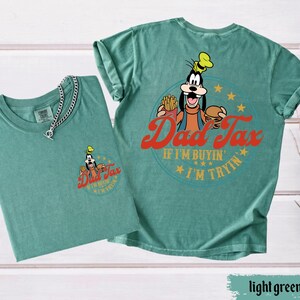 May include: Two light green t-shirts with a graphic of Goofy holding a burger and fries, with the text "Dad Tax" and "If I'm buyin' I'm tryin'". One shirt has a small graphic on the front, and the other has a large graphic on the back.