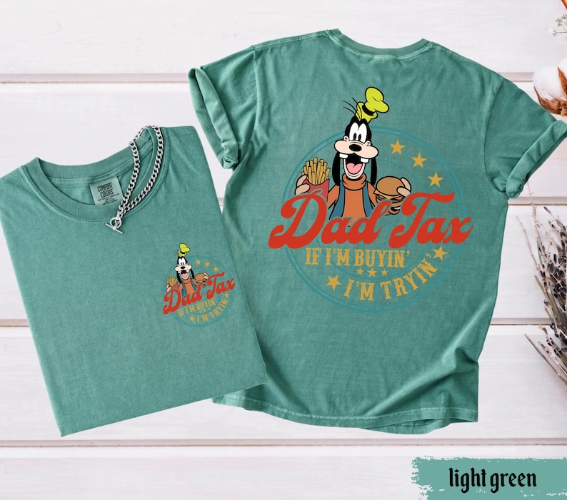 May include: Two light green t-shirts with a graphic of Goofy holding a burger and fries, with the text "Dad Tax" and "If I'm buyin' I'm tryin'". One shirt has a small graphic on the front, and the other has a large graphic on the back.