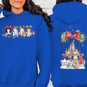 May include: Royal blue hoodie featuring a watercolor design of Disney princesses on the front and back. The front displays four princesses with Mickey Mouse ears and candy canes. The back showcases Cinderella's castle and fireworks.