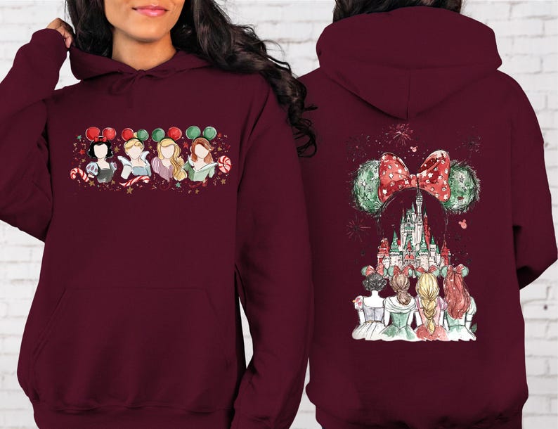 May include: Burgundy hoodie featuring a front graphic of four cartoon princesses with Mickey Mouse ears and candy canes. The back of the hoodie displays a castle with a Minnie Mouse bow and ears, and fireworks.