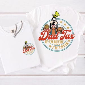 May include: Two white t-shirts with a cartoon graphic of Goofy holding a burger and fries, with the text "Dad Tax". One shirt has a small graphic on the chest, the other has a large graphic. A silver chain necklace is on the smaller shirt.