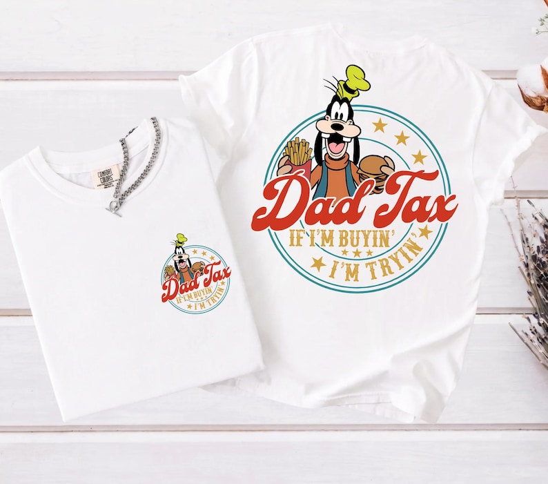 May include: Two white t-shirts with a cartoon graphic of Goofy holding a burger and fries, with the text "Dad Tax". One shirt has a small graphic on the chest, the other has a large graphic. A silver chain necklace is on the smaller shirt.