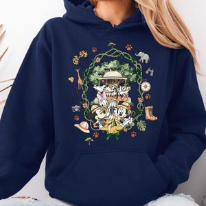 Peut inclure: Sweat &agrave; capuche bleu marine avec un motif sur le th&egrave;me du safari. Le motif comprend des personnages de dessins anim&eacute;s, un v&eacute;hicule de safari et des ic&ocirc;nes de safari telles qu'une boussole, des bottes et un appareil photo. Le motif est entour&eacute; d'une couronne florale.