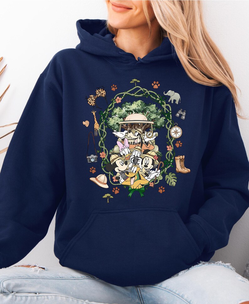Peut inclure: Sweat &agrave; capuche bleu marine avec un motif sur le th&egrave;me du safari. Le motif comprend des personnages de dessins anim&eacute;s, un v&eacute;hicule de safari et des ic&ocirc;nes de safari telles qu'une boussole, des bottes et un appareil photo. Le motif est entour&eacute; d'une couronne florale.