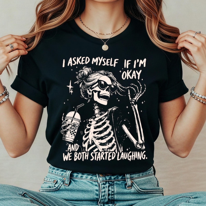 May include: Black t-shirt featuring a skeleton wearing sunglasses and holding a drink. The text on the shirt reads, "I asked myself if I'm okay, and we both started laughing."