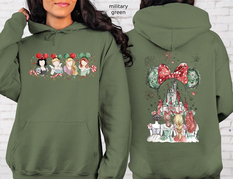 May include: Military green hoodie featuring a front graphic of Disney princesses with candy canes and mouse ears. The back displays a castle, fireworks, and a large bow with mouse ears. A festive design.