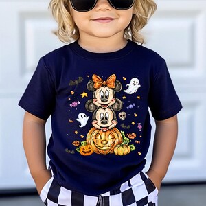 Puede incluir: Camiseta azul marino con un dise&ntilde;o de Halloween. El gr&aacute;fico incluye personajes apilados de Mickey y Minnie Mouse, una calabaza tallada, fantasmas, murci&eacute;lagos y caramelos. El dise&ntilde;o es en tonos naranja, blanco y negro.