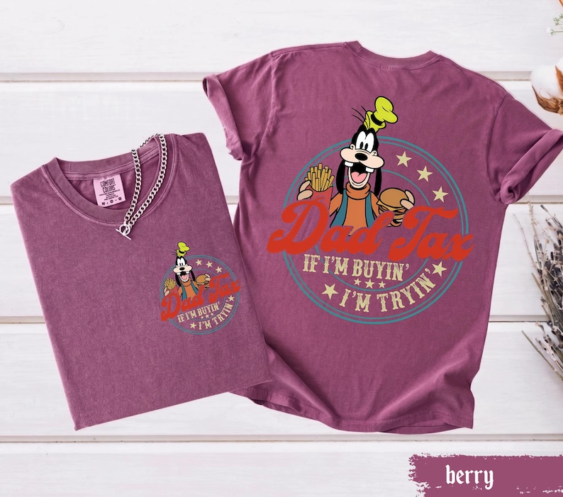 May include: Two berry-colored t-shirts. One shirt has a small graphic of Goofy holding fries and a burger, with text that reads "IF I'M BUYIN' I'M TRYIN'". The other shirt has a larger graphic of Goofy with the text "Dad Tax" and "IF I'M BUYIN' I'M TRYIN'".