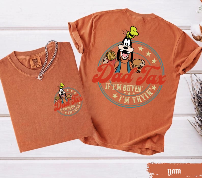 May include: Two orange-brown t-shirts. One shirt has a small graphic of Goofy holding fries and a burger with the text "Dad Tax". The other shirt has a larger version of the same graphic and text. The text reads "If I'm buyin', I'm tryin'."