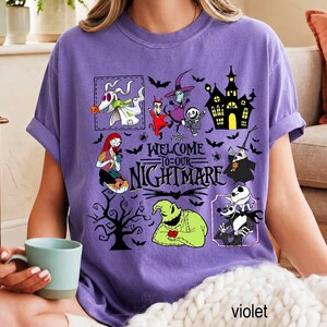 May include: A purple t-shirt featuring a graphic print with the text "WELCOME TO OUR NIGHTMARE" surrounded by various characters and elements from The Nightmare Before Christmas, including Zero, Sally, Oogie Boogie, and a haunted house.