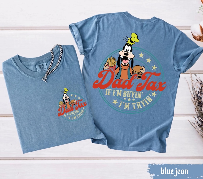 May include: Two blue jean t-shirts. One shirt has a small graphic of Goofy with the text "Dad Tax" and "If I'm buyin', I'm tryin'". The other shirt has a larger graphic of Goofy with the same text. A silver chain necklace is on the first shirt.