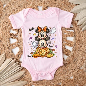 Puede incluir: Un body de beb&eacute; rosa claro con un dise&ntilde;o de Halloween. El dise&ntilde;o incluye a Mickey y Minnie Mouse, una calabaza tallada, fantasmas, murci&eacute;lagos y caramelos. El body tiene mangas cortas y cierres de presi&oacute;n.