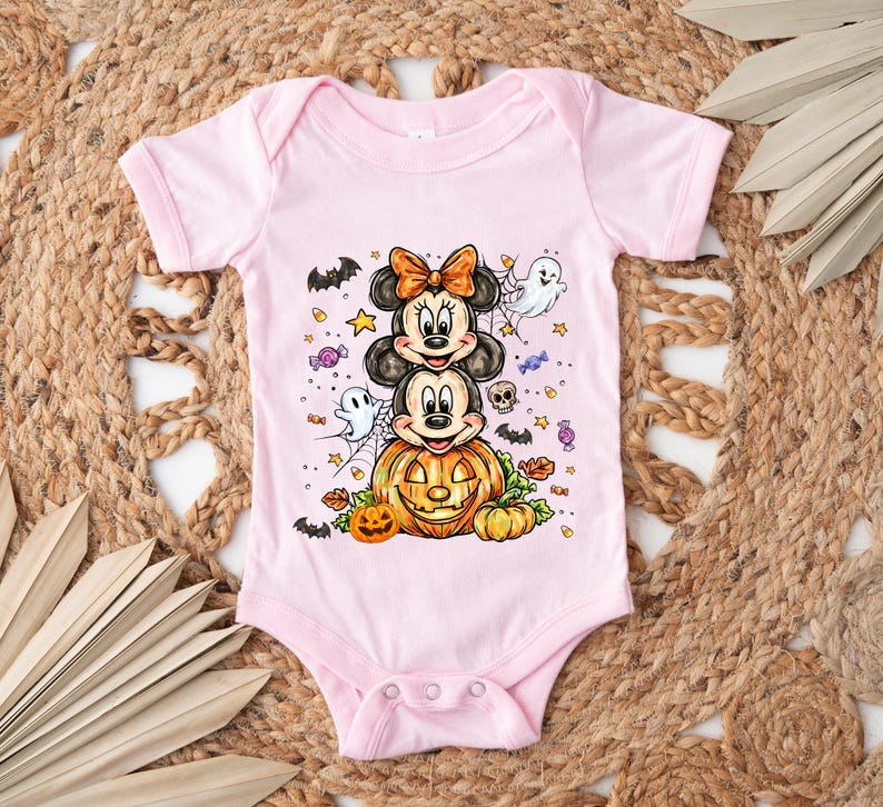 Puede incluir: Un body de beb&eacute; rosa claro con un dise&ntilde;o de Halloween. El dise&ntilde;o incluye a Mickey y Minnie Mouse, una calabaza tallada, fantasmas, murci&eacute;lagos y caramelos. El body tiene mangas cortas y cierres de presi&oacute;n.