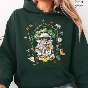 Peut inclure: Sweat &agrave; capuche vert for&ecirc;t avec un motif sur le th&egrave;me du safari repr&eacute;sentant des personnages de dessins anim&eacute;s, dont Mickey Mouse et Donald Duck. Le motif comprend des chapeaux de safari, des jumelles et des illustrations d'animaux. Le texte "forest green" est imprim&eacute; en haut &agrave; droite.