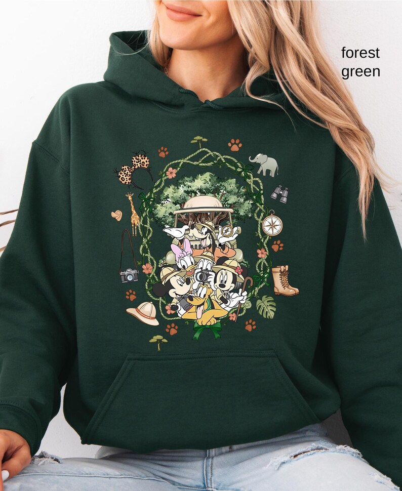 Peut inclure: Sweat &agrave; capuche vert for&ecirc;t avec un motif sur le th&egrave;me du safari repr&eacute;sentant des personnages de dessins anim&eacute;s, dont Mickey Mouse et Donald Duck. Le motif comprend des chapeaux de safari, des jumelles et des illustrations d'animaux. Le texte "forest green" est imprim&eacute; en haut &agrave; droite.