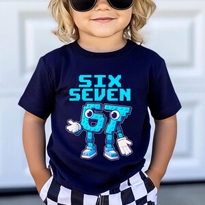 May include: A navy blue t-shirt with the words "SIX SEVEN" in pixelated blue letters. Below, the numbers "6" and "7" are depicted as cartoon characters with arms, legs, and shoes. The child is wearing sunglasses and checkered shorts.