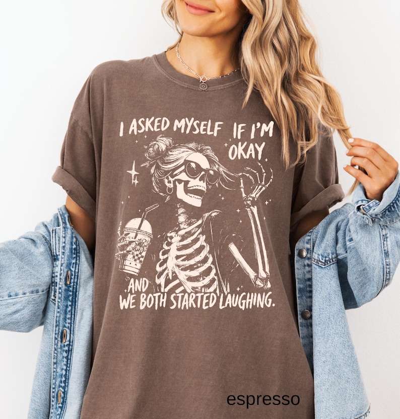 May include: Espresso-colored t-shirt featuring a skeleton wearing sunglasses and holding a drink. The graphic includes the text "I asked myself if I'm okay and we both started laughing."