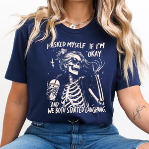 May include: Navy blue t-shirt featuring a skeleton wearing sunglasses and holding a beverage. The graphic includes the text "I asked myself if I'm okay and we both started laughing."