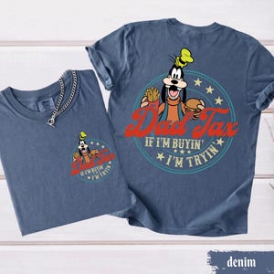 May include: Two denim blue t-shirts. One shirt has a small graphic of Goofy with the text "Dad Tax" and "If I'm buyin', I'm tryin'". The other shirt has a larger version of the same graphic.