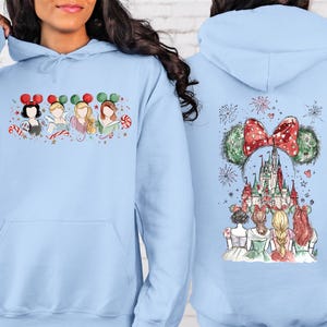 May include: Light blue hoodie featuring a watercolor design of Disney princesses with Mickey Mouse ears and candy canes on the front. The back of the hoodie displays a castle, fireworks, and more princesses.