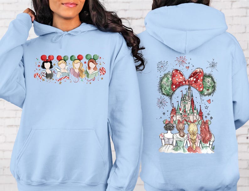 May include: Light blue hoodie featuring a watercolor design of Disney princesses with Mickey Mouse ears and candy canes on the front. The back of the hoodie displays a castle, fireworks, and more princesses.