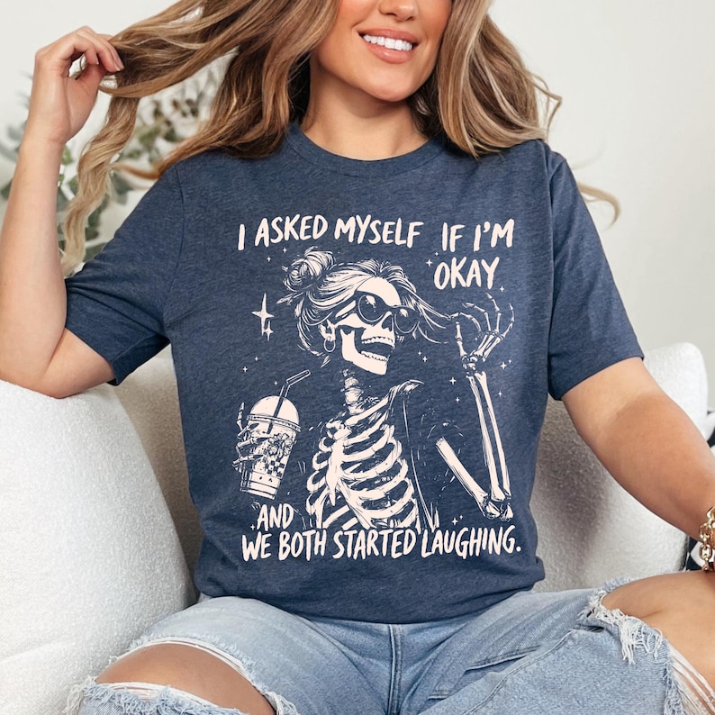 May include: Navy blue t-shirt with a skeleton graphic wearing sunglasses and holding a drink. The text reads, "I asked myself if I'm okay. And we both started laughing."