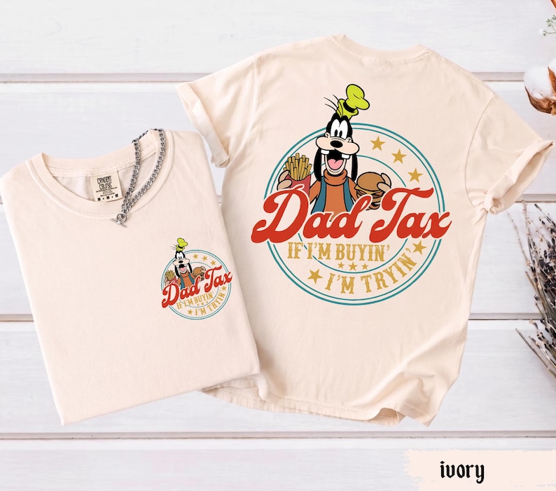 May include: Ivory-colored t-shirts featuring a cartoon character holding a burger and fries, with the text "Dad Tax" in red script. The design is repeated on the front pocket and back of the shirts. The shirts have a round neckline and short sleeves.