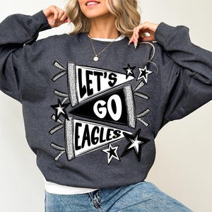 May include: Dark gray sweatshirt with the text "LET'S GO EAGLES" in a pennant design, accented with black and white stars. The sweatshirt is a comfortable, casual style.