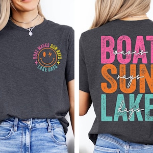 May include: Dark grey t-shirt with the words "BOAT WAVES SUN RAYS LAKE DAYS" in a colourful design. The front features a smiley face graphic. The back of the shirt displays the same text in a stacked layout.