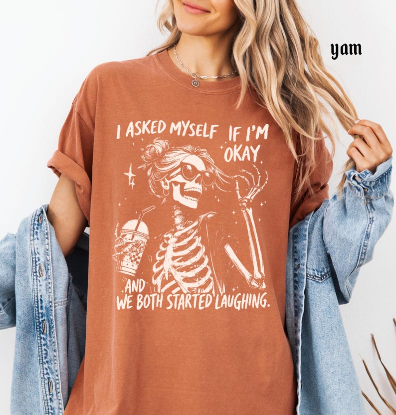 May include: Rust-colored t-shirt featuring a skeleton graphic with sunglasses and a drink, along with the text "I asked myself if I'm okay, and we both started laughing."
