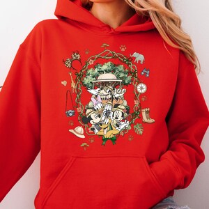 Peut inclure: Sweat &agrave; capuche rouge avec un motif de safari. Le motif comprend un chapeau de safari, des jumelles, une boussole et un appareil photo. Le motif est entour&eacute; d'une couronne de feuilles et d'animaux de safari.