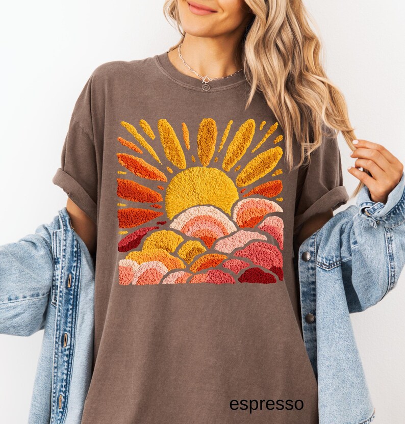 May include: Espresso-colored t-shirt featuring an embroidered sun design in shades of yellow, orange, and red. The shirt has a relaxed fit and rolled sleeves. The word "espresso" is printed at the bottom.