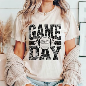 Puede incluir: Camiseta color crema con las palabras "GAME DAY" en letras negras desgastadas, con un gr&aacute;fico de f&uacute;tbol americano. La camiseta es de estilo casual, adecuada para el d&iacute;a del partido o el uso diario.