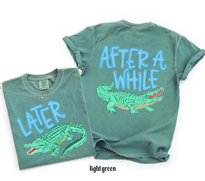 May include: Two light green t-shirts with alligator graphics. One shirt says "LATER" and the other says "AFTER A WHILE" in light blue. The alligators are green with red mouths and yellow bellies.