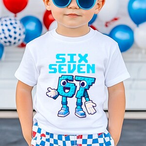 May include: White t-shirt with the words "SIX SEVEN" in pixelated blue font. Below the text are the numbers 6 and 7 designed as cartoon characters in blue, with white gloves and shoes. The shirt is worn by a child.
