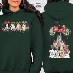 May include: Forest green hoodie featuring a festive design. The front displays princess illustrations with candy canes and balloons. The back showcases a castle, bow, and mouse ears. A cozy and stylish garment.