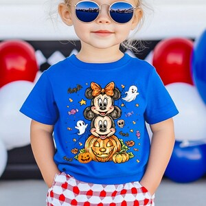 Puede incluir: Una camiseta azul de manga corta con un dise&ntilde;o de Halloween. El gr&aacute;fico incluye a Minnie y Mickey Mouse apilados encima de una calabaza tallada, rodeados de fantasmas, murci&eacute;lagos y caramelos. Llevada por un ni&ntilde;o.